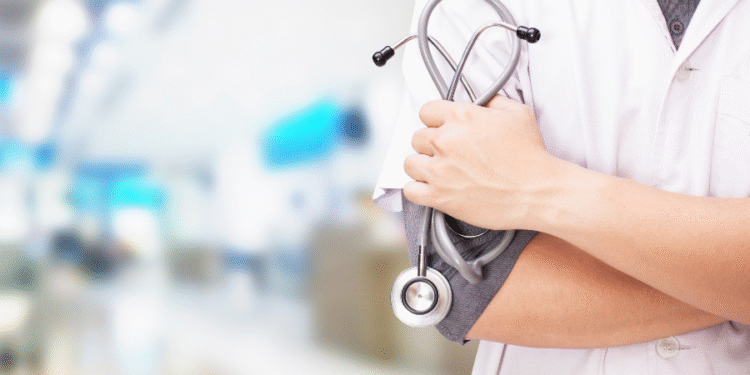 Un profesional de la salud con un estetoscopio cruzado sobre el brazo, en un entorno de hospital desenfocado.