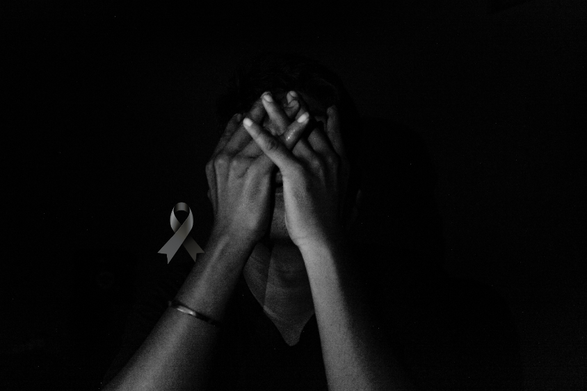 Une personne les mains sur le visage, dans un environnement sombre, avec un ruban noir superposé à l'image.