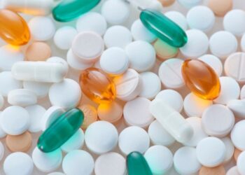 Una variedad de píldoras y cápsulas de diferentes colores y formas, incluyendo tabletas blancas, naranjas y verdes, dispuestas sobre una superficie clara.