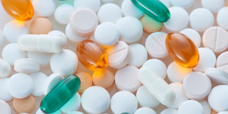 Una variedad de píldoras y cápsulas de diferentes colores y formas, incluyendo tabletas blancas, naranjas y verdes, dispuestas sobre una superficie clara.