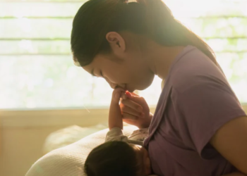Una madre amamantando a su bebé, con luz natural que entra por la ventana, capturando un momento íntimo entre ambos.